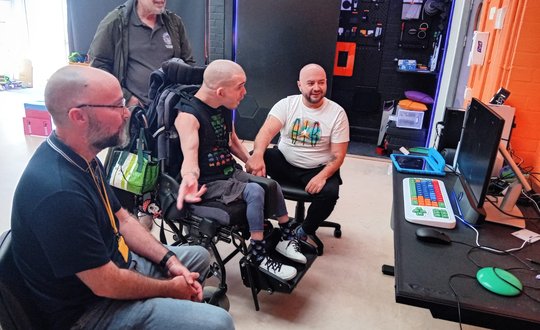 Group of 4 men playing accessible space invaders via a head switch controller.