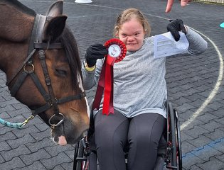 Young person in a wheelchair with horse and rosette