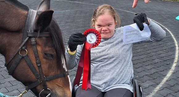Young person in a wheelchair with horse and rosette