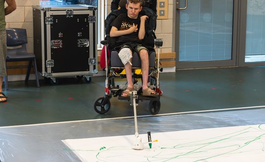 Boy using adaptive equipment to his wheelchair to paint.