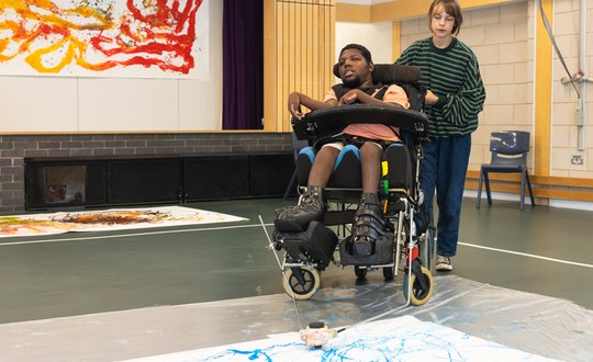 Boy using adaptive equipment to his wheelchair to paint.