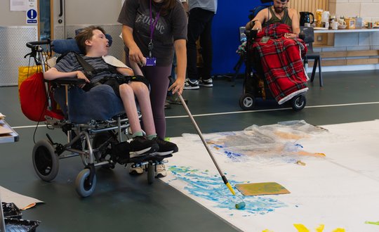 Boy using adaptive equipment to his wheelchair to paint.