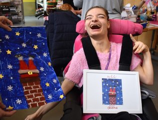 Young girl holding a frame with Christmas card in next to her big Christmas design of Santa's legs down a chimney, made of paint and cotton wool