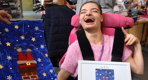 Young girl holding a frame with Christmas card in next to her big Christmas design of Santa's legs down a chimney, made of paint and cotton wool