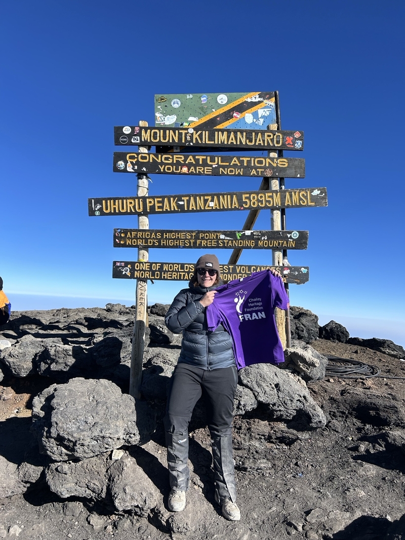 lady holding up Chailey branded T-shirt on top of a mountain.