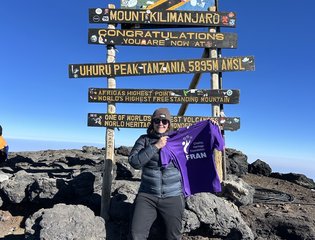lady holding up Chailey branded T-shirt on top of a mountain.