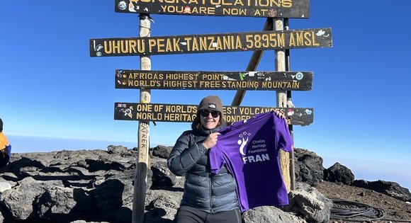 lady holding up Chailey branded T-shirt on top of a mountain.