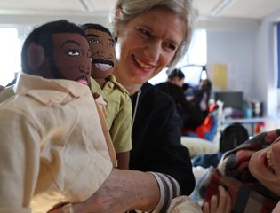Women holding up dolls to a young person.