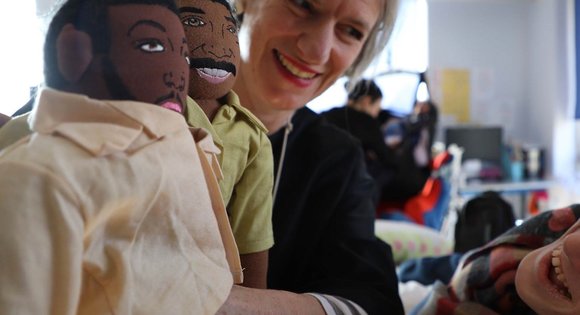 Women holding up dolls to a young person.