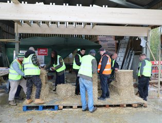 a group of people being taught how to use bales of straw to build a structure