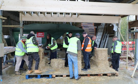 a group of people being taught how to use bales of straw to build a structure