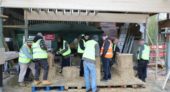 a group of people being taught how to use bales of straw to build a structure