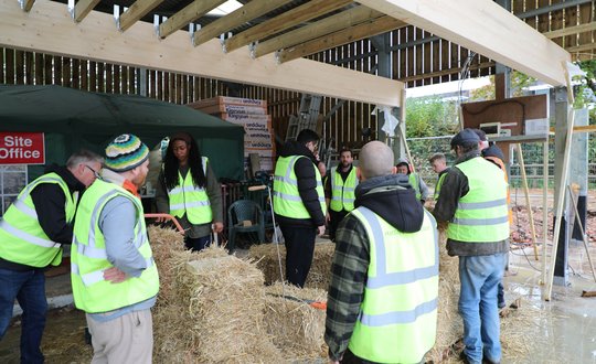a group of people being taught how to use bales of straw to build a structure
