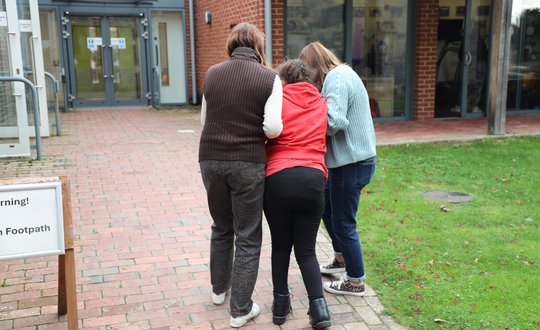 Girl walking with the help from two women.
