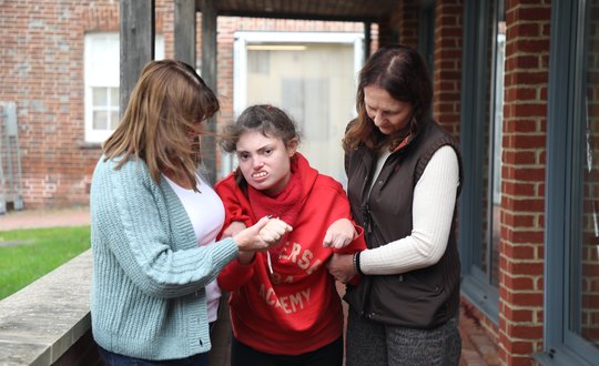 Girl walking with the help from two women.