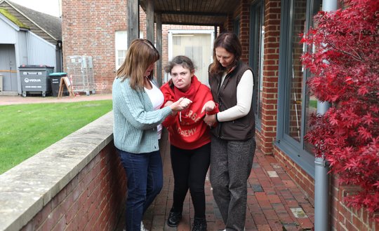 Girl walking with the help from two women.