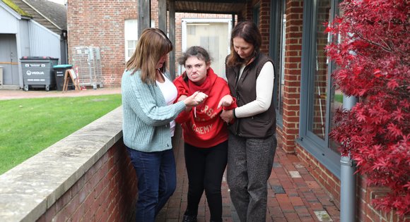 Girl walking with the help from two women.