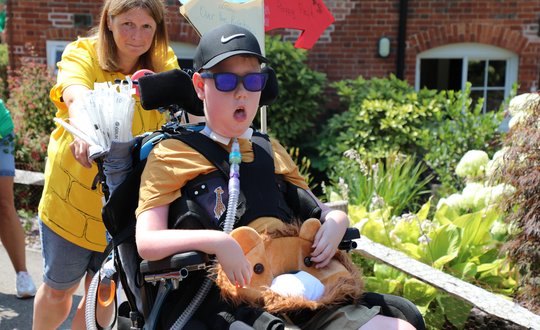 Boy dressed up being wheeled by his support worker.
