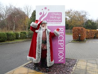 Father Christmas standing in front of a Chailey Heritage Foundation sign