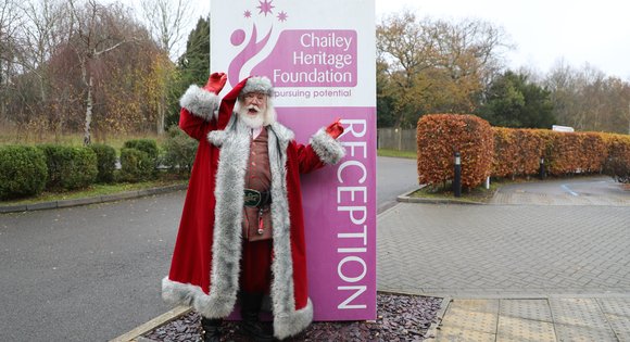 Father Christmas standing in front of a Chailey Heritage Foundation sign