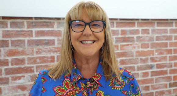 Women smiling with glasses and a blue blouse.
