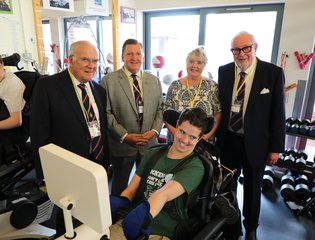 Group of club members crowded by a user using a adaptive gym bike.