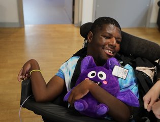 Boy smiling with a purple teddy bear.