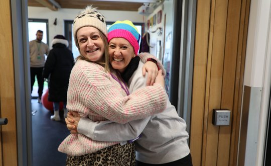 two workers hugging and smiling with woolly hats on.