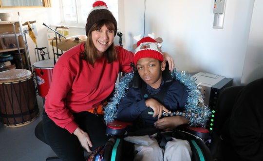 Support worker and young boy smiling at the camera with woolly hats.