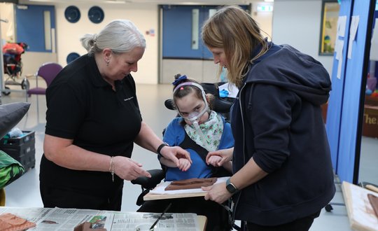 Girl sculpting clay with help of support workers.