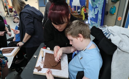 Boy with support worker sculpting clay.