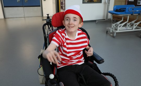 Young boy dressed up in a stripped shirt pointing and smiling at the camera.