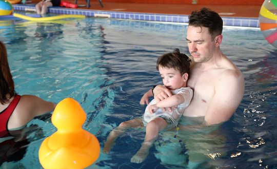 Young boy and dad in the pool with a gaint rubber duck.