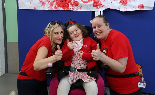 Young girl and two support workers smiling with thumbs up dressed in red.