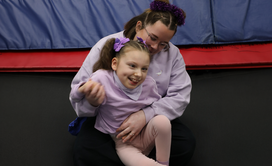 Young girl dressed in purple on a trampoline.
