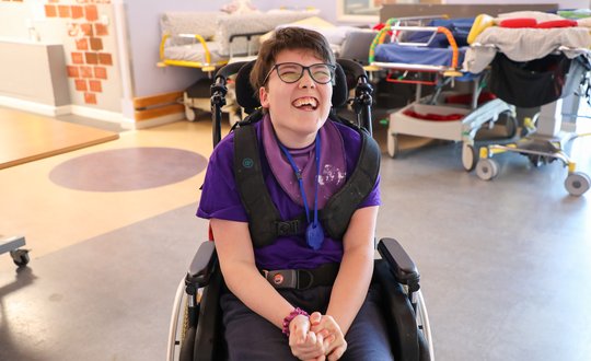 Girl smiling in her chair dressed in purple.