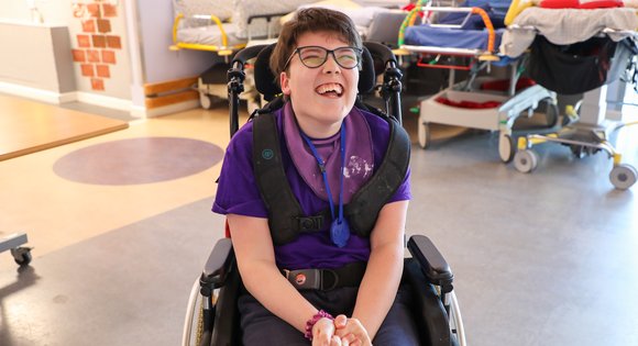 Girl smiling in her chair dressed in purple.