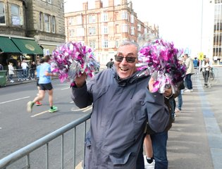 Man smiling with pompoms cheering on runners.