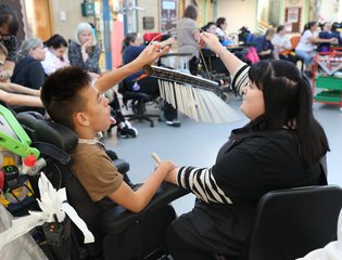 Young boy and support worker playing with a musical instrument.