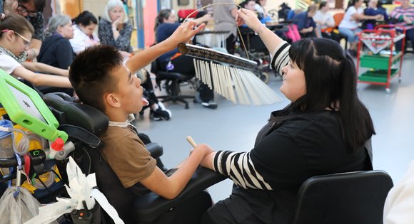 Young boy and support worker playing with a musical instrument.