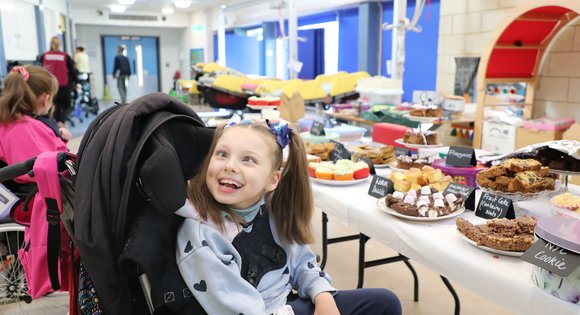 Young girl smiling by lots of cakes.