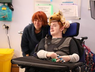 young boy in wolf hat holding a bell wrist instrument with support worker