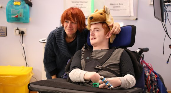 young boy in wolf hat holding a bell wrist instrument with support worker
