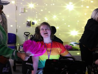 Girl with a colourful top smiling at the camera with projector lights behind her.