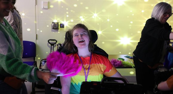Girl with a colourful top smiling at the camera with projector lights behind her.