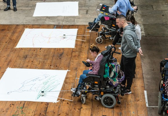 Girl using adaptive drawing equipment attached to a wheelchair.