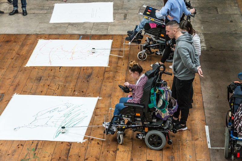 Girl using adaptive drawing equipment attached to a wheelchair.