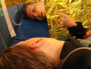 Young person laying down looking in a mirror in sensory art.