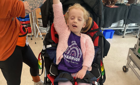 Young girl raising her arm while wearing a purple top.