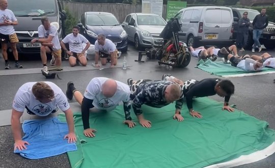 Men doing push ups outside in a car park.